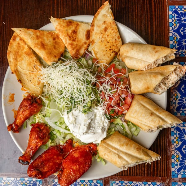 Happy Mexican's platter with quesadillas, flautas, chicken wings, lettuce, shredded cheese, pico de gallo, and sour cream.