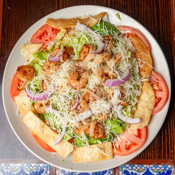 Happy Mexican shrimp salad with lettuce, tomatoes, red onions, cheese, and tortilla strips.