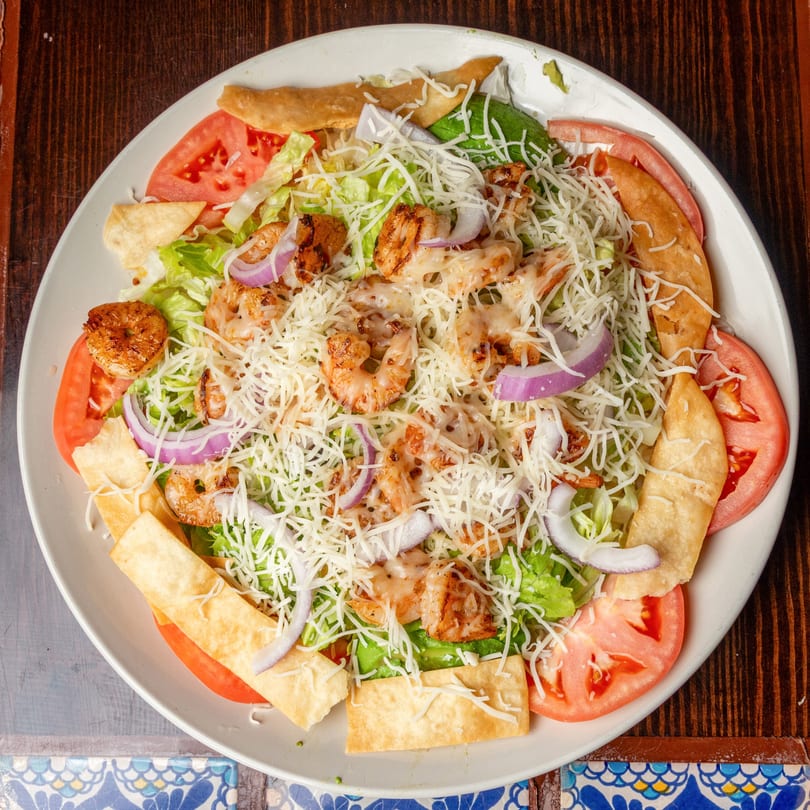 Happy Mexican shrimp salad with lettuce, tomatoes, red onions, cheese, and tortilla strips.