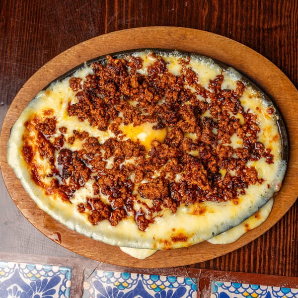 Happy Mexican's melted cheese with chorizo in a sizzling skillet on a wooden board.