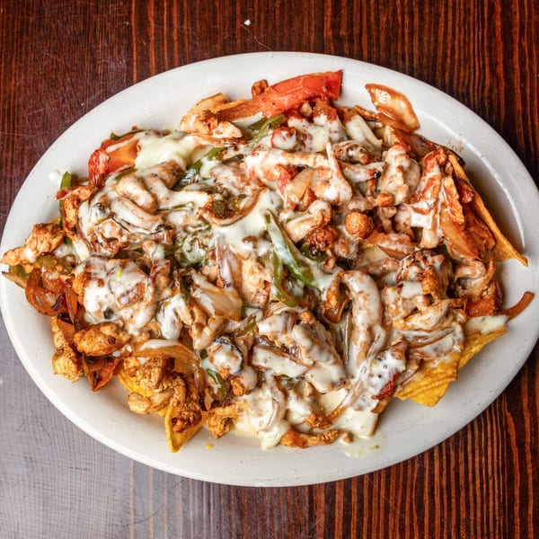 Happy Mexican's chicken nachos with melted white cheese, peppers, and onions on a white plate.