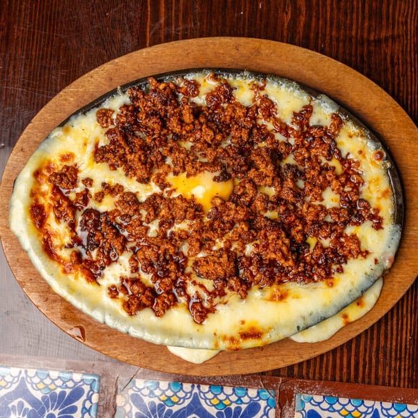 Happy Mexican's melted cheese with chorizo in a sizzling skillet on a wooden board.