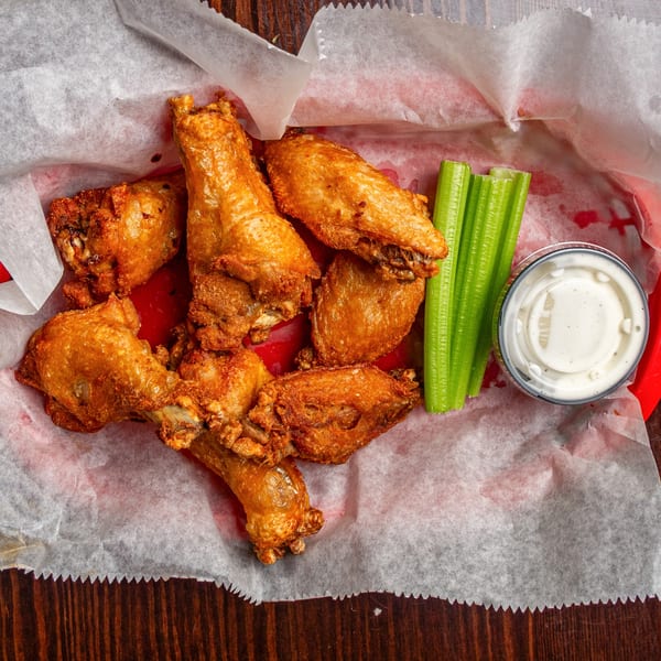 Happy Mexican's crispy fried chicken wings with celery sticks and ranch dressing in a red basket.